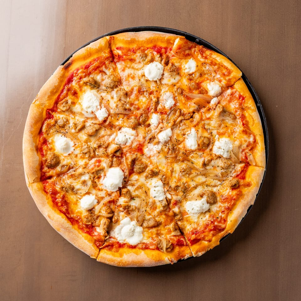 Round pizza with tomato sauce, melted cheese, sausage, onions, and dollops of ricotta cheese.
