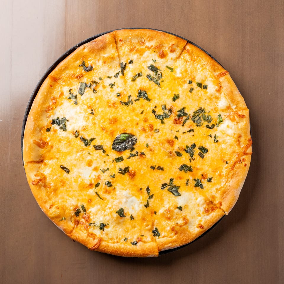 Overhead view of a whole cheese pizza with basil, sliced and ready to eat.