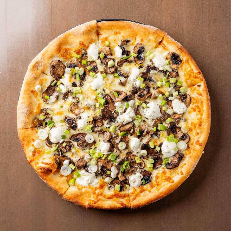 Round mushroom and ricotta pizza, topped with sliced green onions, on a brown surface.