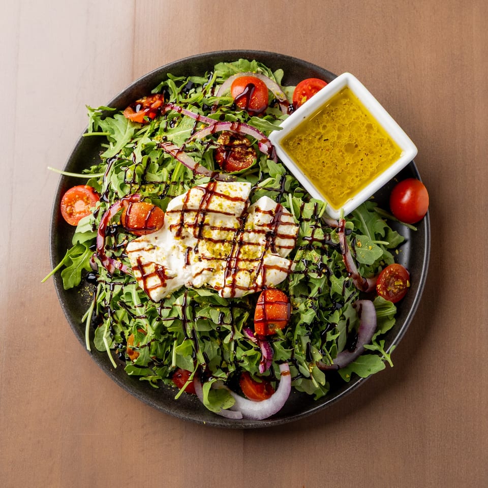 Arugula salad with burrata, cherry tomatoes, red onion, balsamic glaze, and a side of vinaigrette.