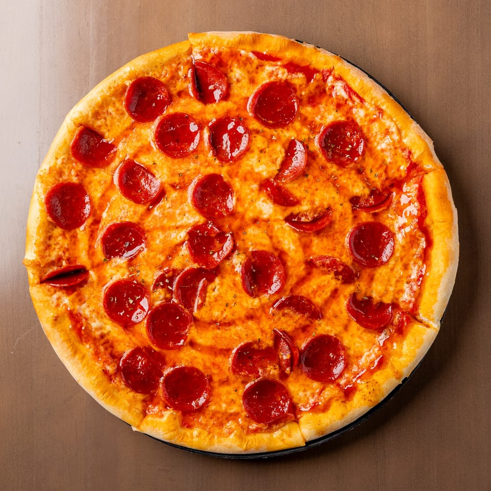 A whole pepperoni pizza with melted cheese and a golden crust on a dark surface.
